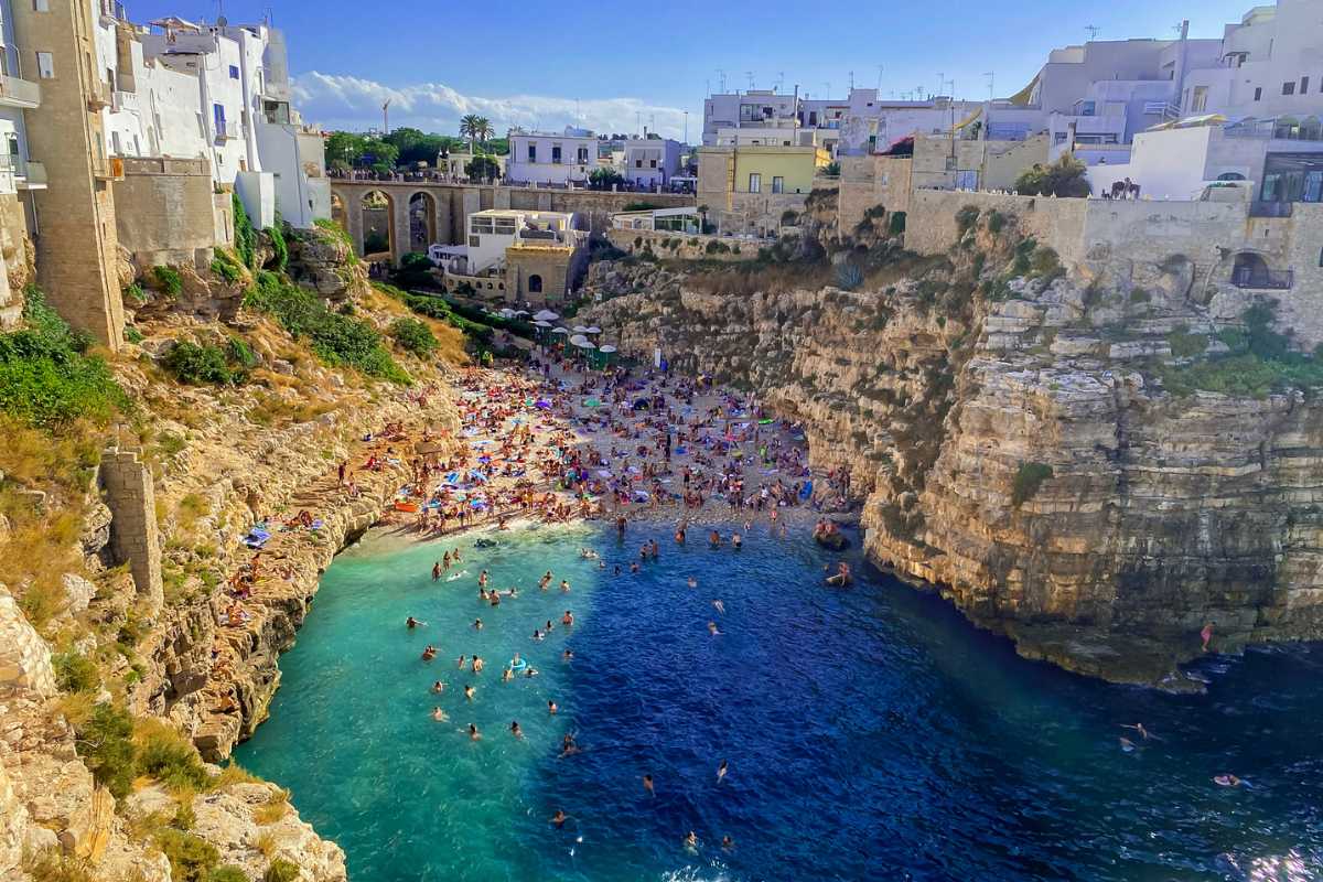 Panorama ampio della spiaggia di Lama Monachile a Polignano a Mare, vista dall'alto con scogliera, acqua cristallina e centro storico sullo sfondo